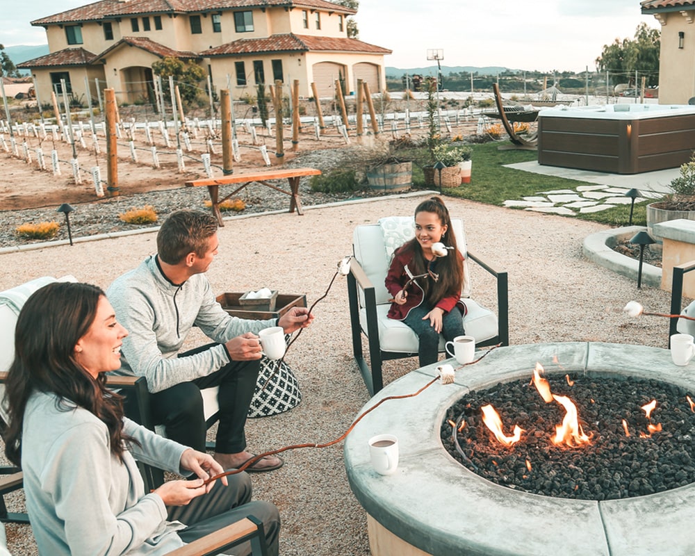 Three people enjoying an outdoor fire pit seating area with hot tub in the background